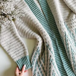 A hand holding a crocheted cardigan.