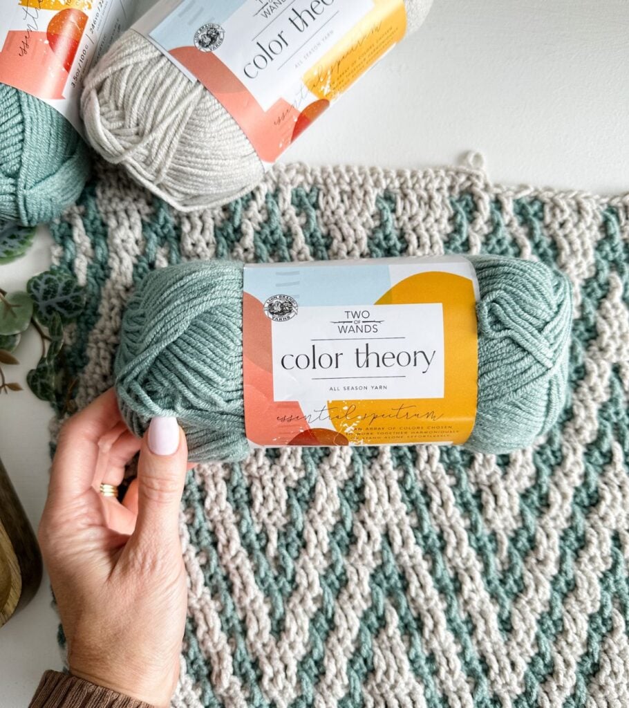 A person holding a ball of yarn next to a rug.