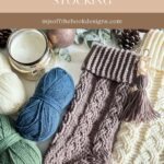 A cabled stocking with a beautiful cable pattern is displayed alongside yarn balls, a candle, pinecones, and a finished cream-colored crocheted item. Text reads: "COZY COTTAGE CABLED STOCKING.