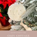 A white Christmas Crochet Ornament bauble hangs on a snow-dusted tree branch, with a red poinsettia and wooden bead garland in the background.