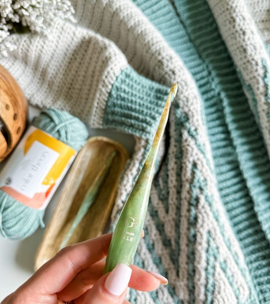 A person holding a knitting needle in front of a blanket.
