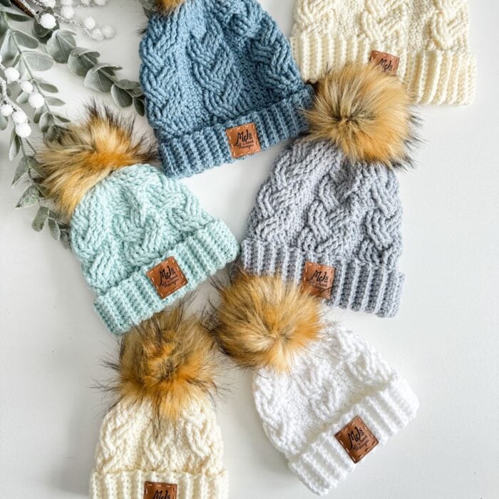 A group of cabled hats with pom poms.