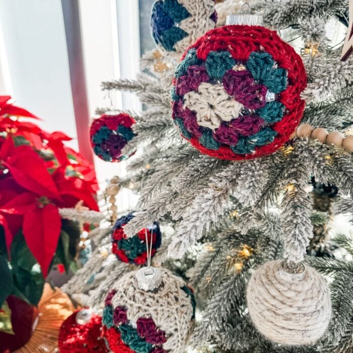 A Christmas tree adorned with crochet ornaments and poinsettias, including crochet stockings.