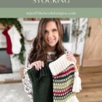 A woman holds two large crocheted holiday stockings, one dark green and one striped, in a cozy living room adorned with festive holiday decorations and a charming granny square ornament.