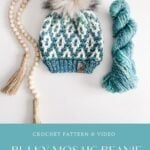 A knitted blue and white beanie with a fur pom-pom, a skein of blue yarn, a beaded tassel garland, and a charming granny square ornament displayed on a white surface.