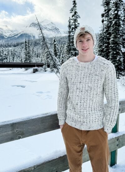A young man wearing a crocheted hat in the snow.