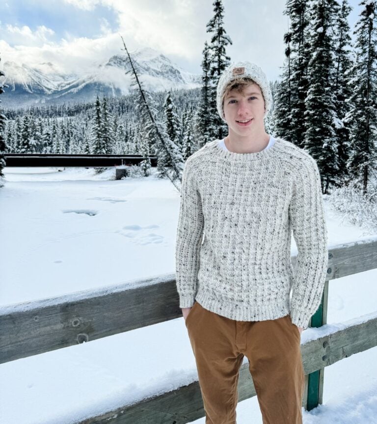 A young man wearing a crocheted hat in the snow.