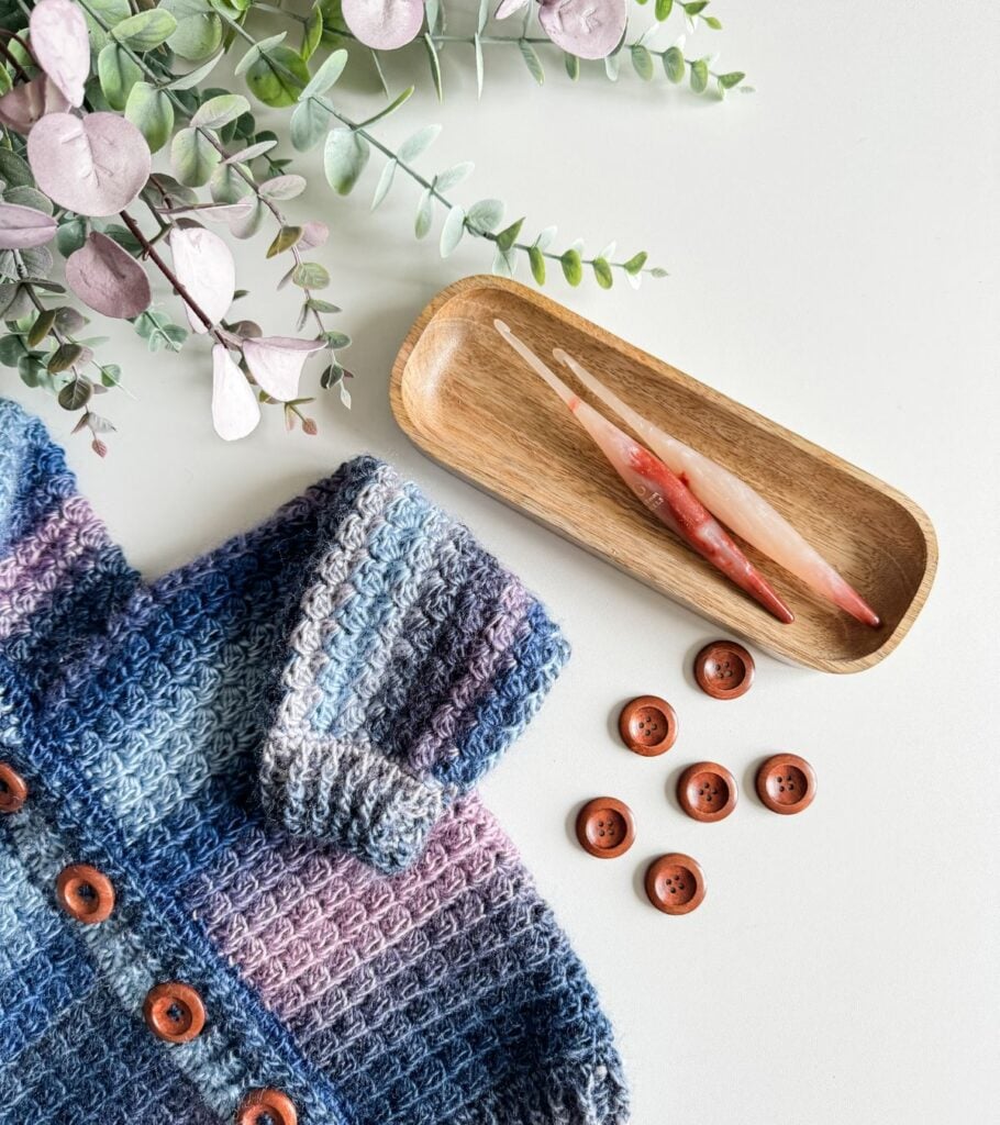 A crocheted cardigan with buttons and flowers on a table.