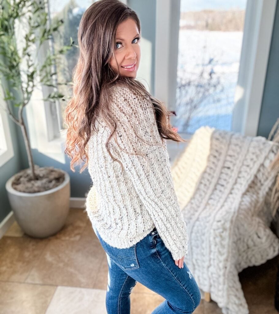 A woman wearing jeans and a sweater, with a crochet hat, in a living room.