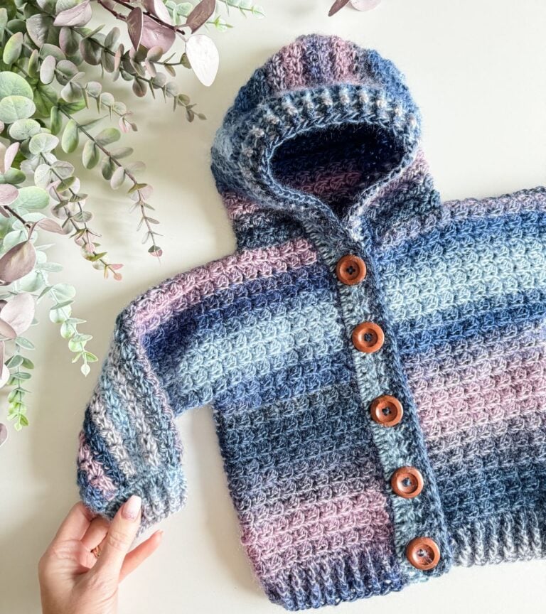 A hand holding a crocheted Granny Stitch hooded jacket.