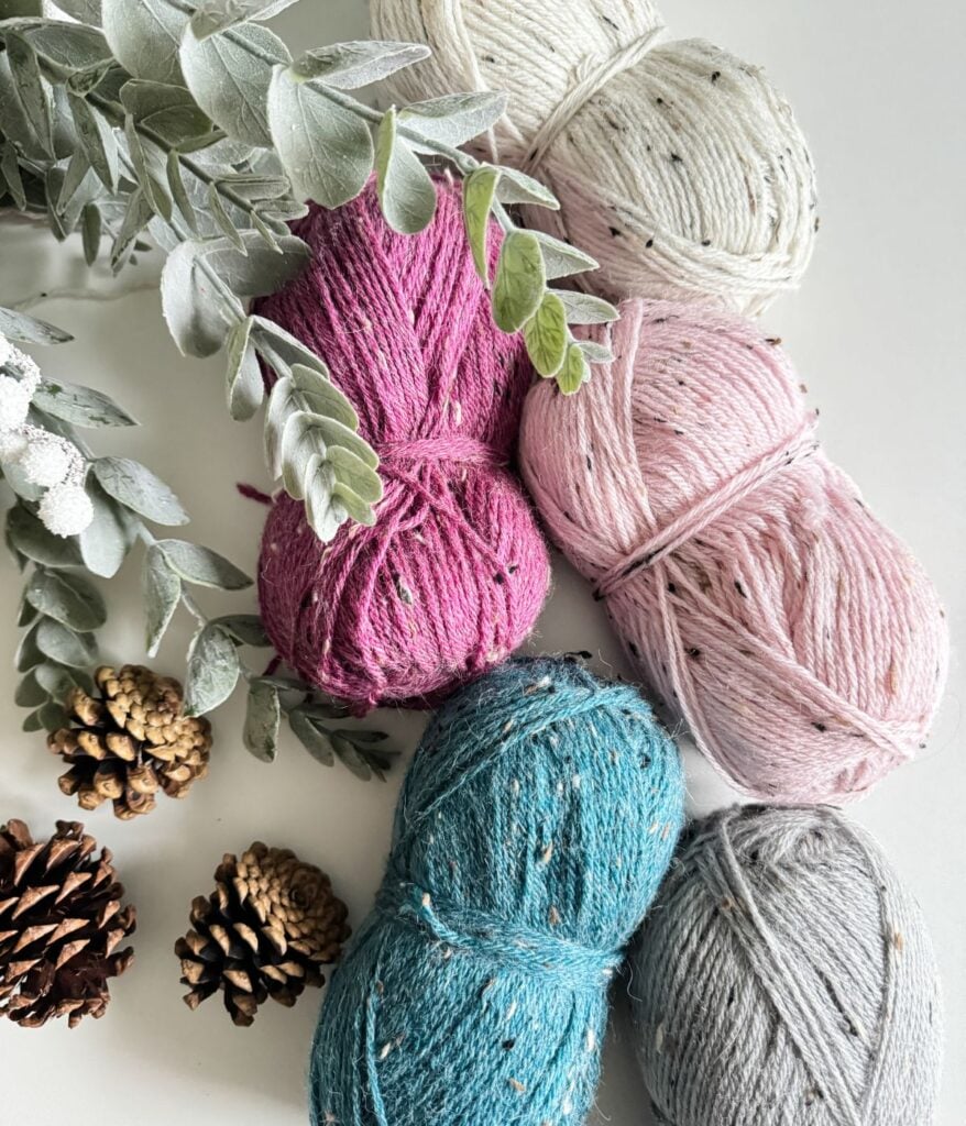 Four balls of yarn with pine cones and pine needles, perfect for creating a cozy Crochet Hat.