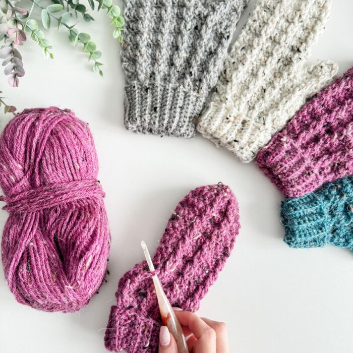 A person crocheting mittens with colorful yarn.