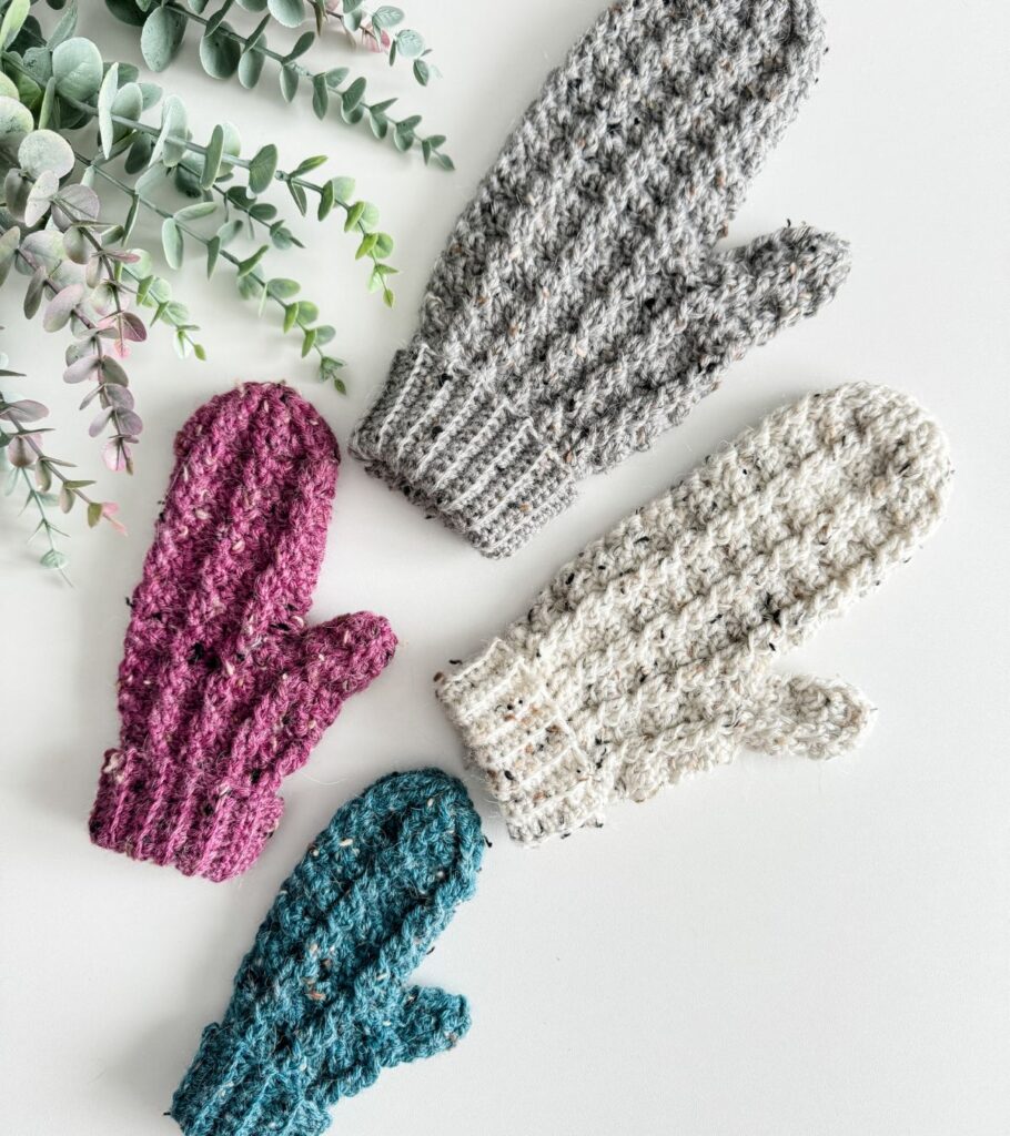Four crocheted mittens on a white surface.