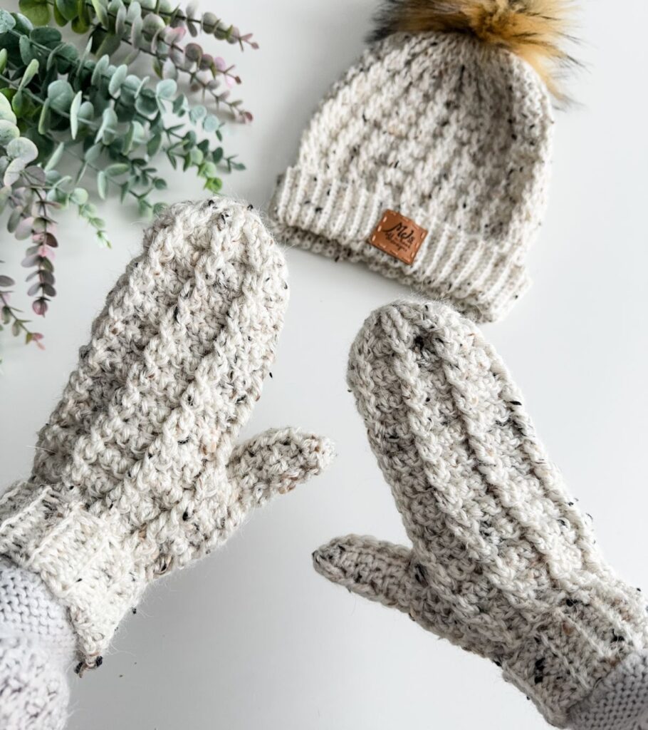 A pair of crocheted mittens and a pom pom hat with a crochet touch.