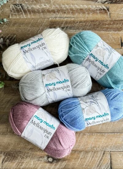 Four balls of yarn resting on a wooden table, ready to be transformed into a cozy children's pullover.