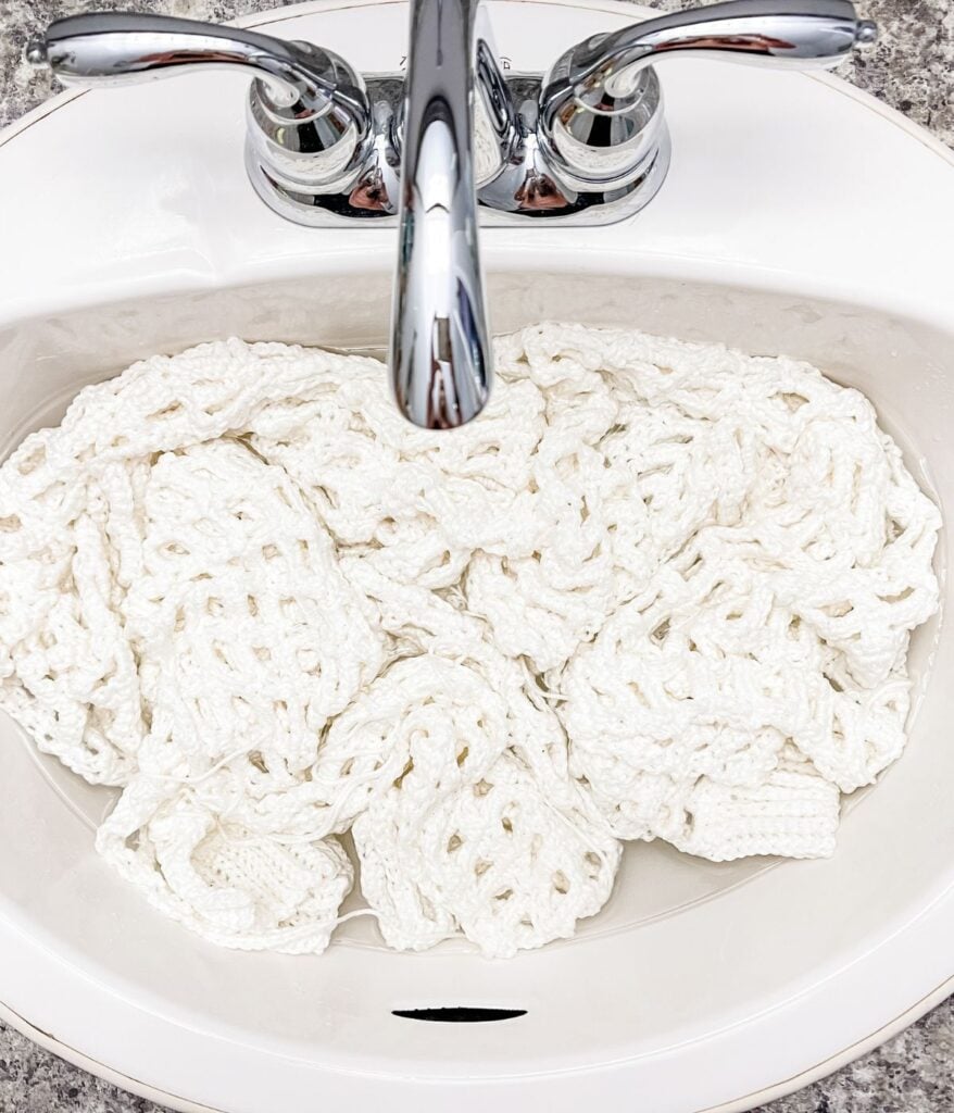 White crochet cardigan soaking in a bathroom sink.