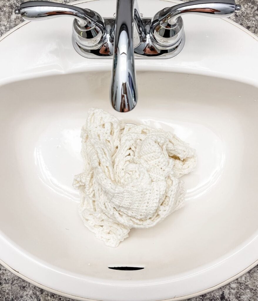 A white crochet cardigan soaking in a bathroom sink.