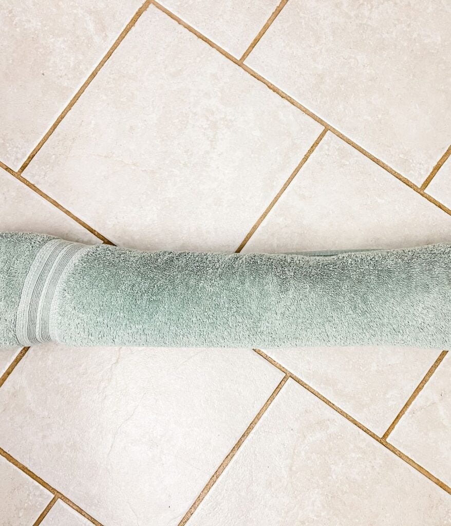 A rolled-up green towel on a tiled floor beside a crochet cardigan.