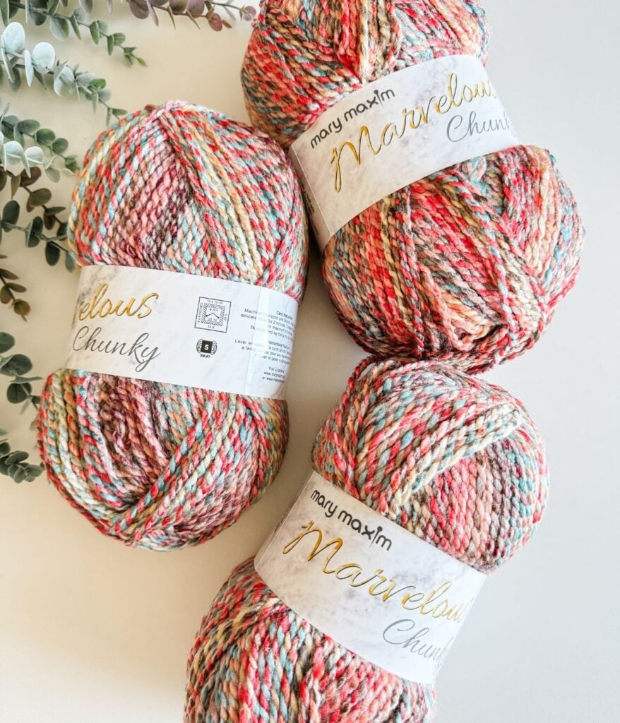 Three balls of yarn on a table next to a crochet pullover.