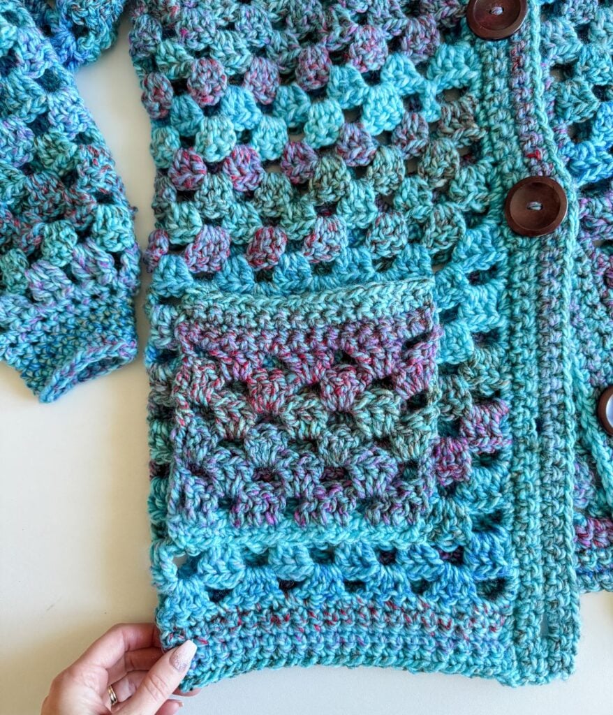 A woman is holding a crocheted cardigan.