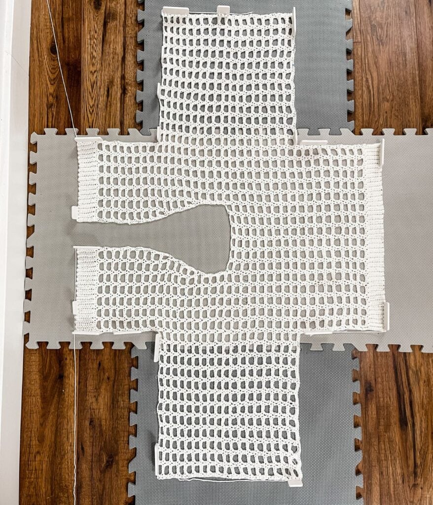 A crocheted white cardigan laid out on interlocking foam mats for blocking.