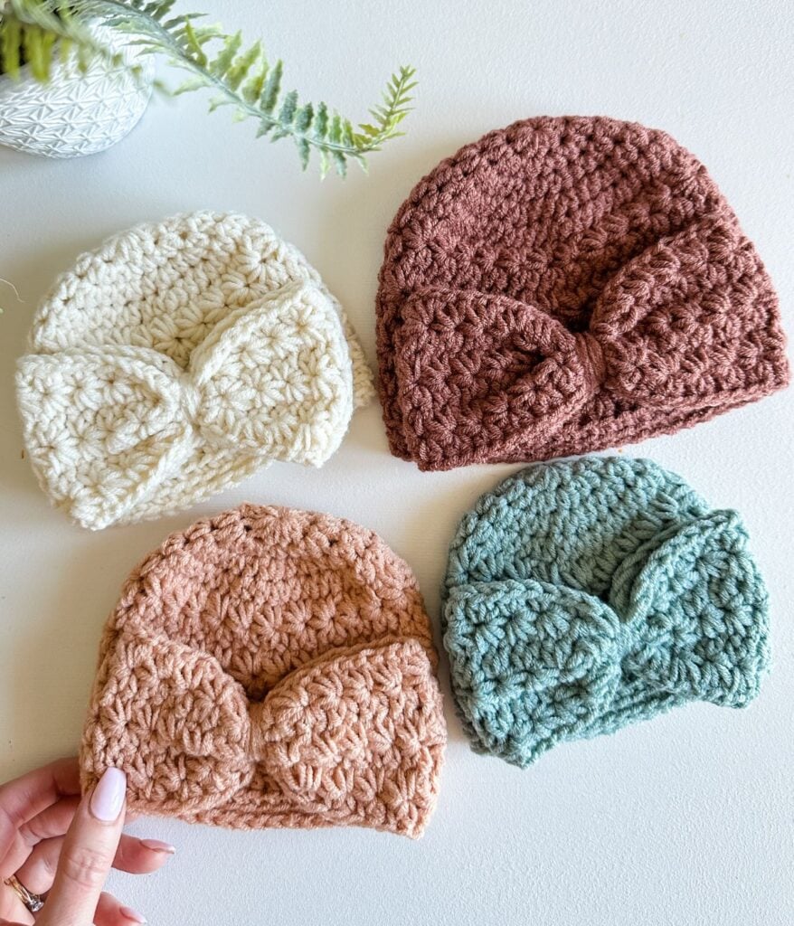 Four crocheted children's beanies with bow embellishments displayed in an array of colors.