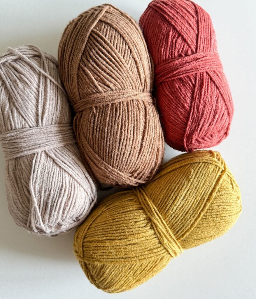 Four balls of yarn in different colors arranged on a white surface.