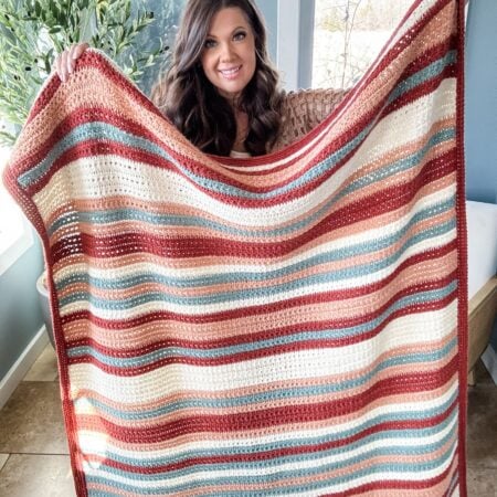 Woman displaying a handmade striped blanket, ideal for crafting the easiest children’s crochet pullover.