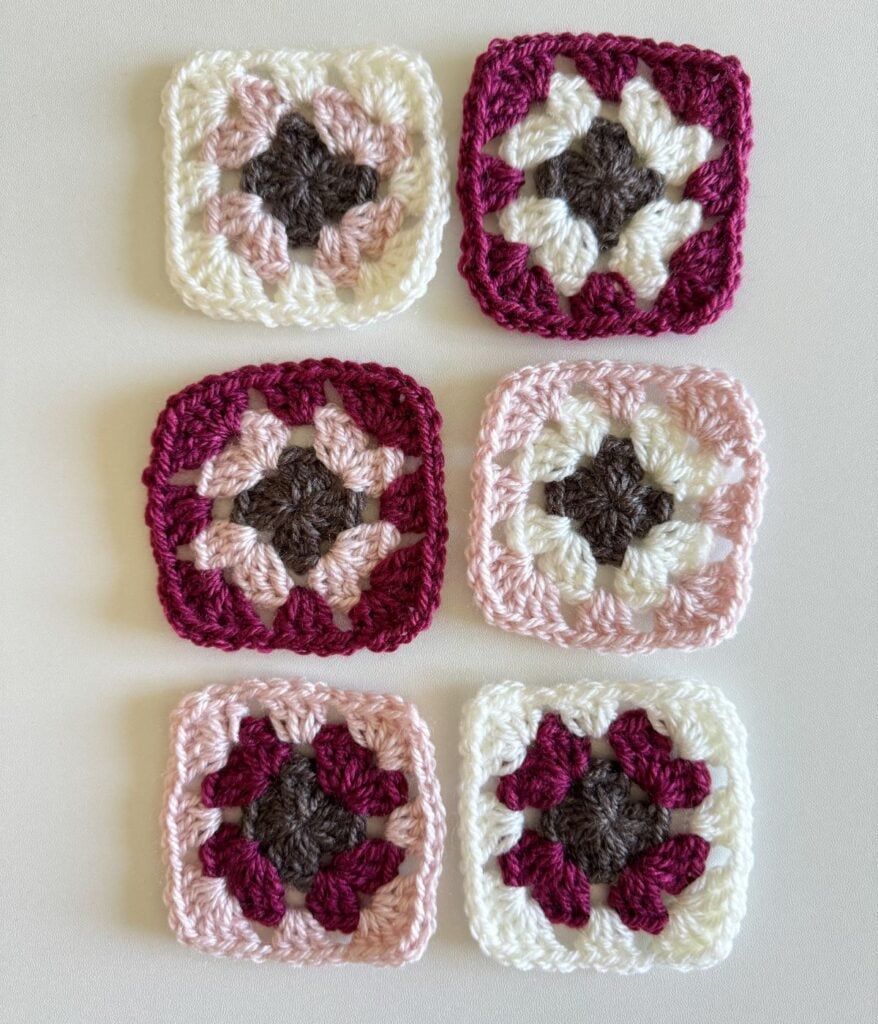 Six crocheted granny squares in various color combinations laid out on a light surface, each featuring a distinct floral pattern.