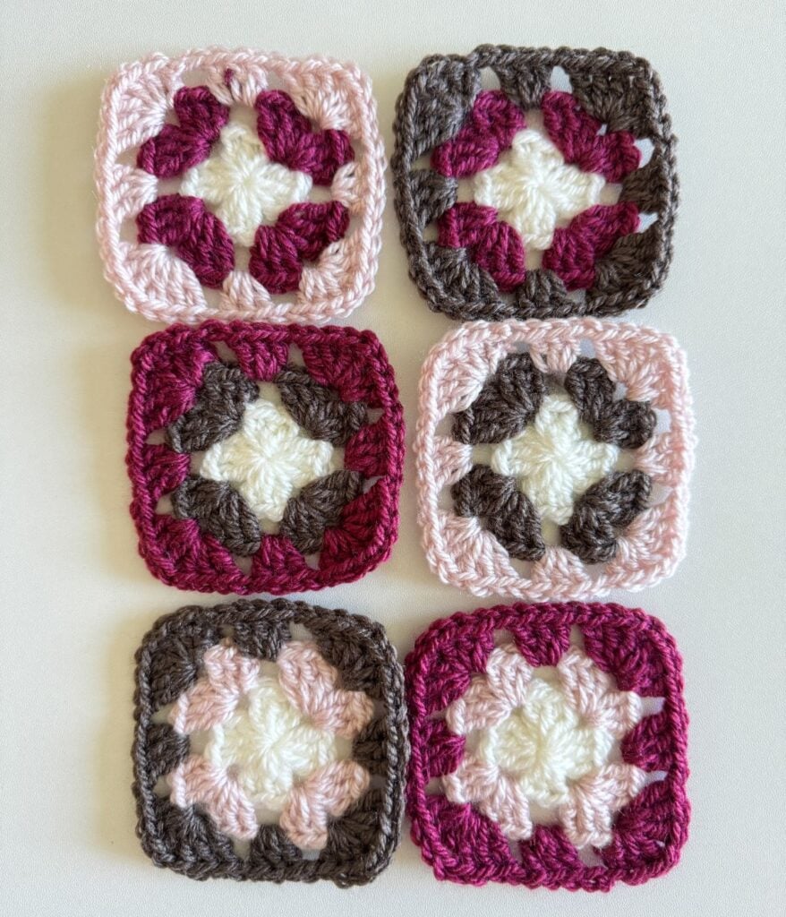 Six crocheted granny squares in assorted colors arranged in two rows on a white background, featuring patterns.