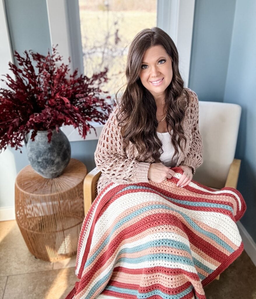 Woman sitting in a chair with the easiest children's crochet pullover, smiling at the camera.