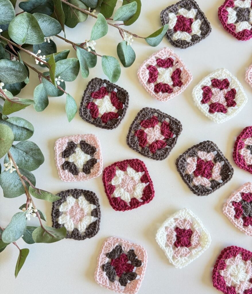 Handmade crochet granny squares in various colors, carefully arranged on a table with eucalyptus leaves.