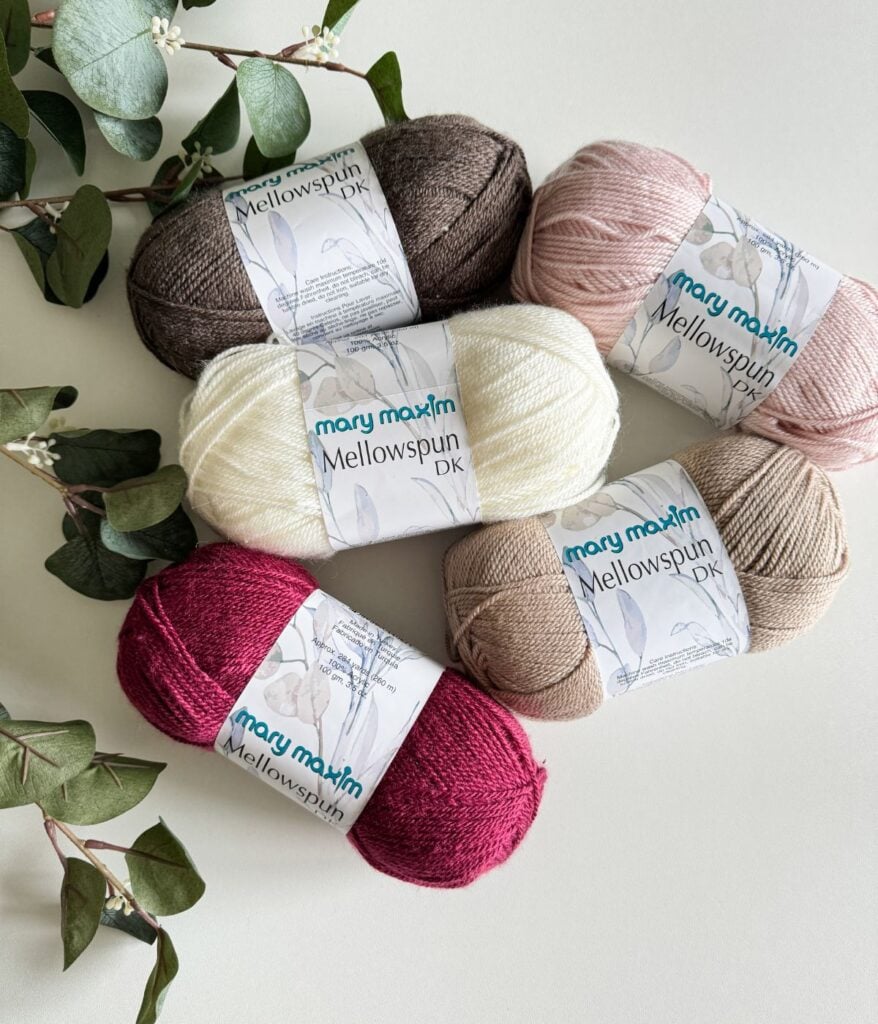 Five skeins of yarn in assorted colors, perfect for granny square projects, alongside green eucalyptus leaves on a light background.