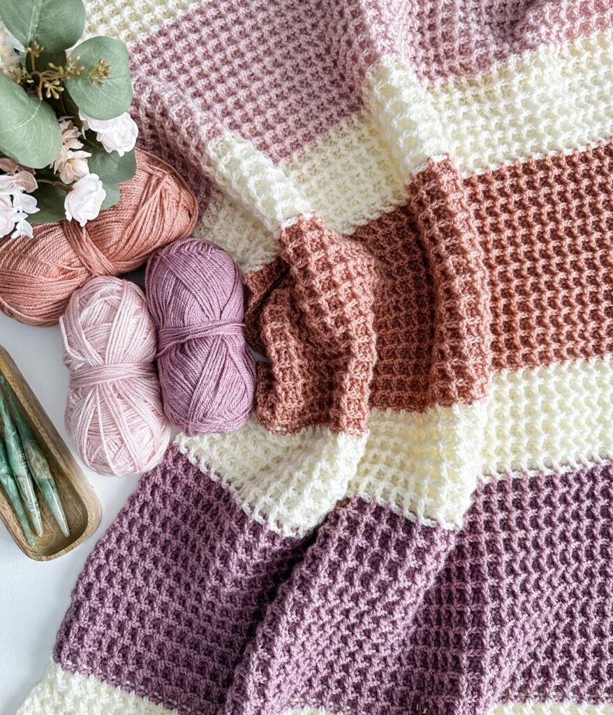 Handmade children's crochet pullover with pink and cream yarn balls and green crochet hooks on a white background.
