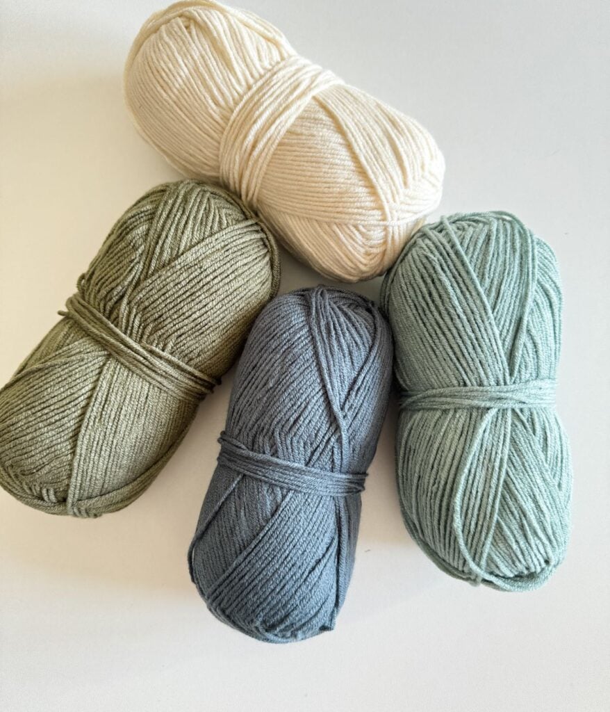Four skeins of yarn in different shades of green and blue on a white background.