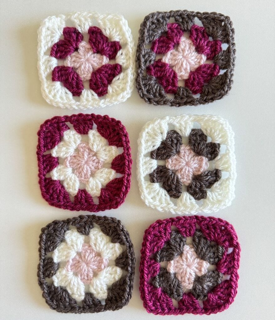 Six crocheted granny squares showcased on a white surface, each featuring a floral pattern in varying shades of pink, burgundy, white, and brown.