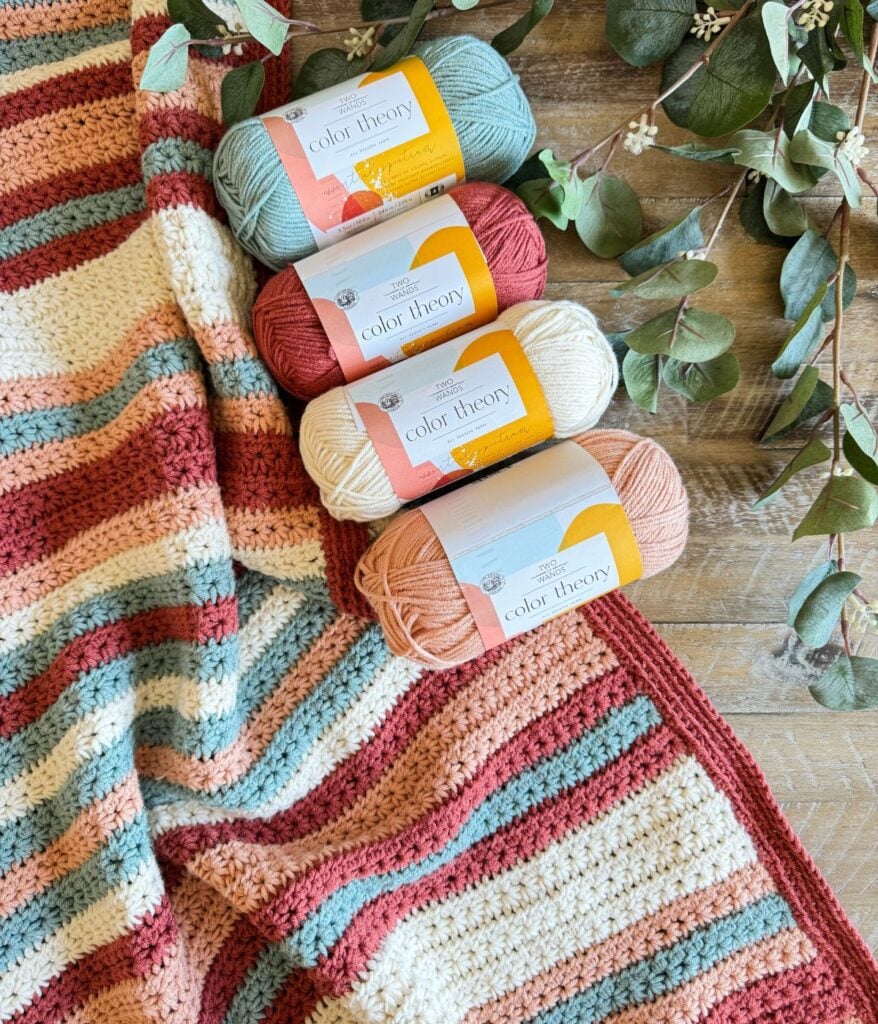 Stack of colorful yarn beside a crocheted children's pullover on a wooden surface.
