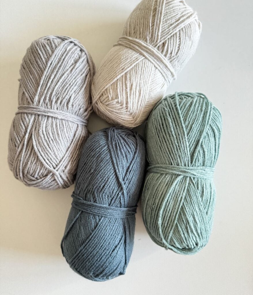 Four skeins of yarn in various shades positioned on a white surface.