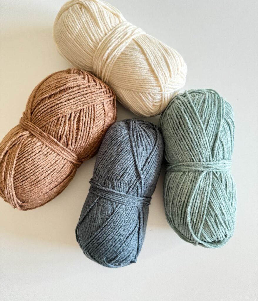 Four skeins of yarn in soft pastel colors arranged on a white background.