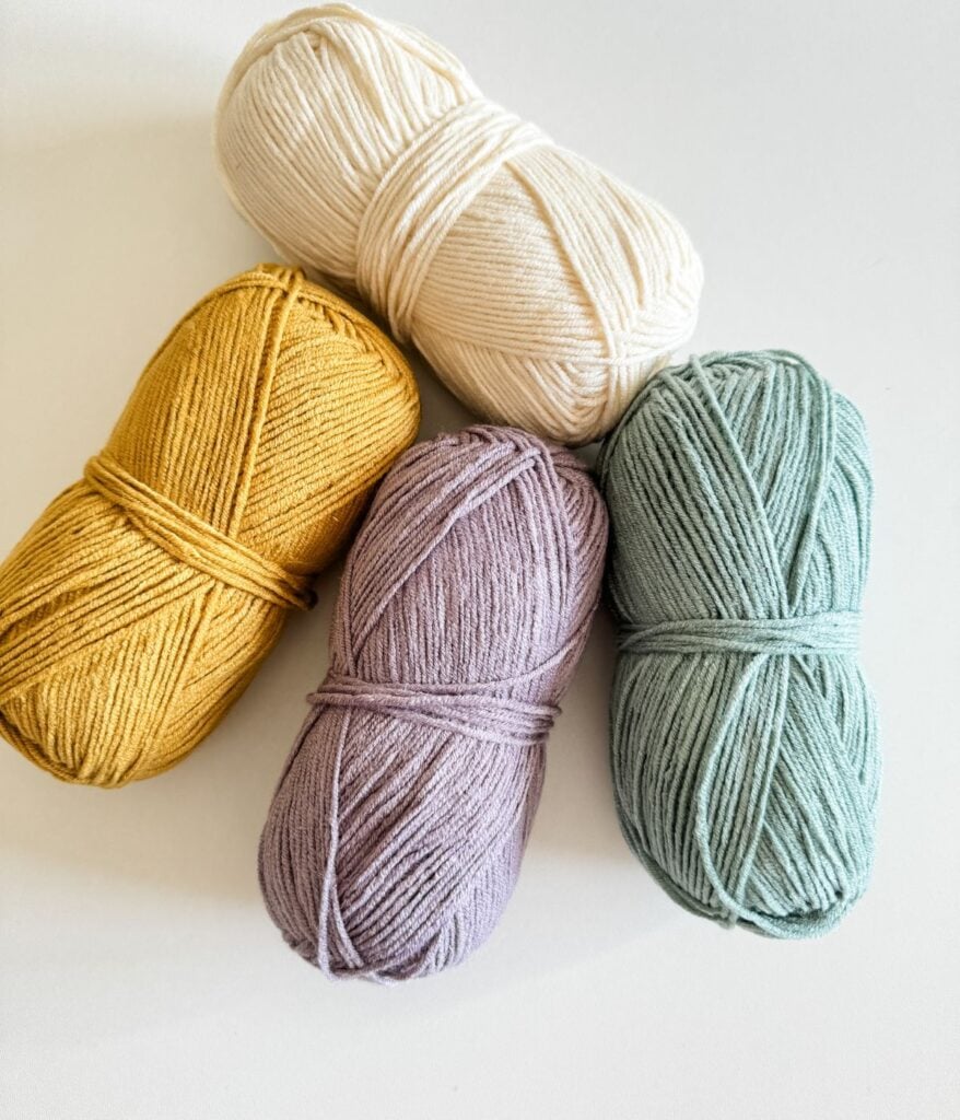 Four skeins of yarn in different colors arranged side by side on a white background.