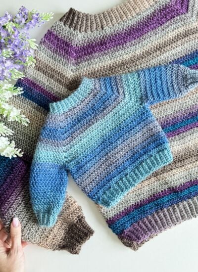 A handcrafted crochet cardigan laid out flat next to purple flowers.