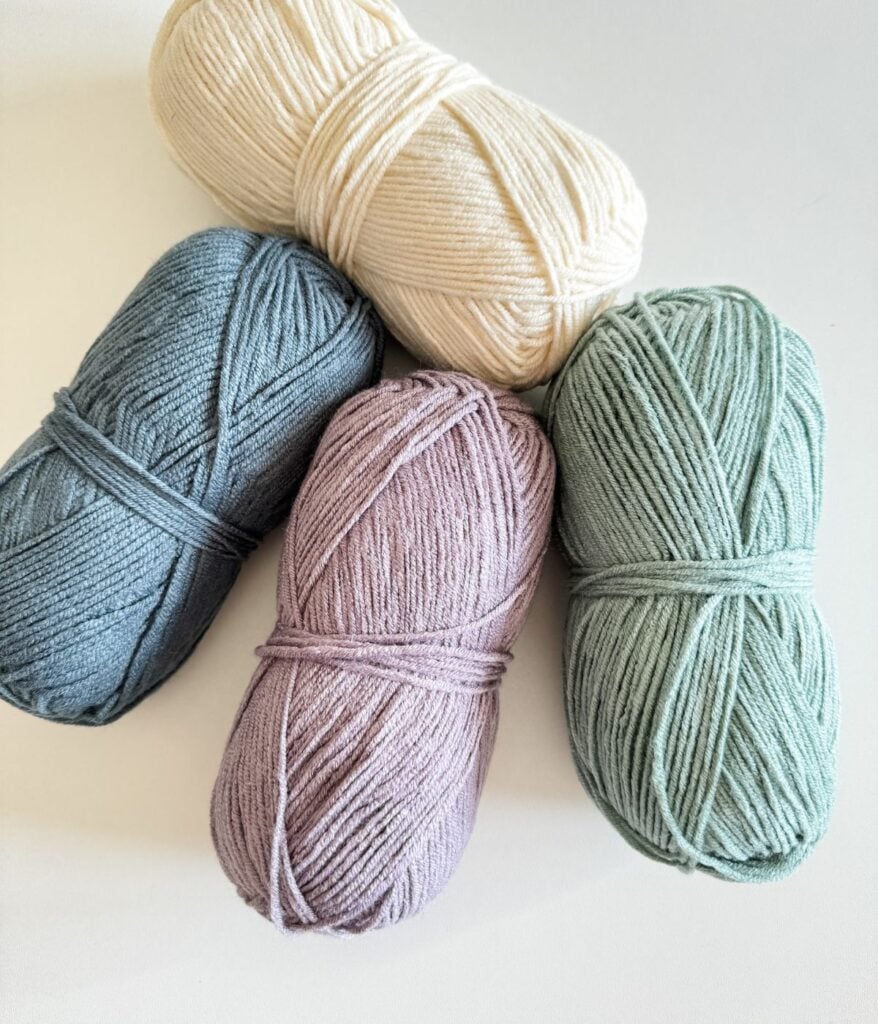 Four skeins of yarn in different pastel colors arranged overlapping each other on a white surface.