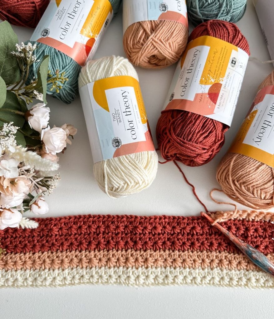 A crochet project in progress for the easiest children's pullover, with a selection of yarn balls and a floral decoration.