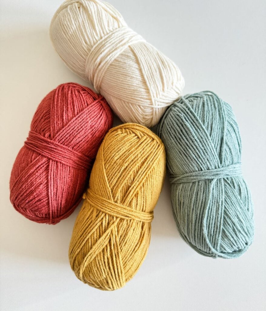 Four skeins of yarn in different colors arranged together on a white surface.