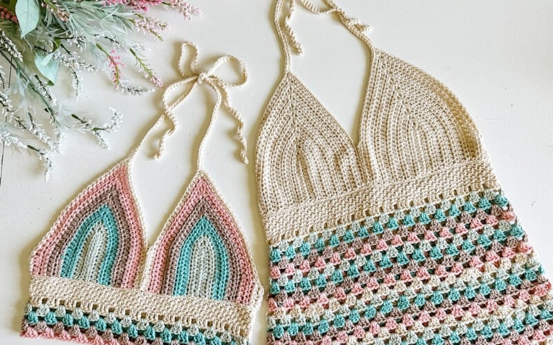 Two crochet patterns for halter tops laid flat, one beige and pink with a teardrop pattern, the other with multicolored horizontal stripes and a beige base.