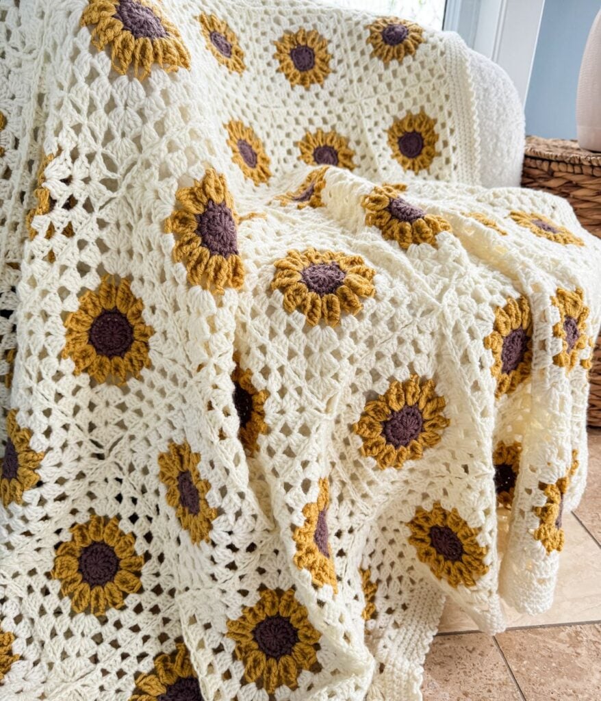 Handmade crochet blanket with white and yellow sunflower patterns draped over a chair in a bright room.