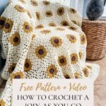 A crocheted sunflower granny square blanket draped over a chair next to a window, with a wicker basket and decorative vase nearby.