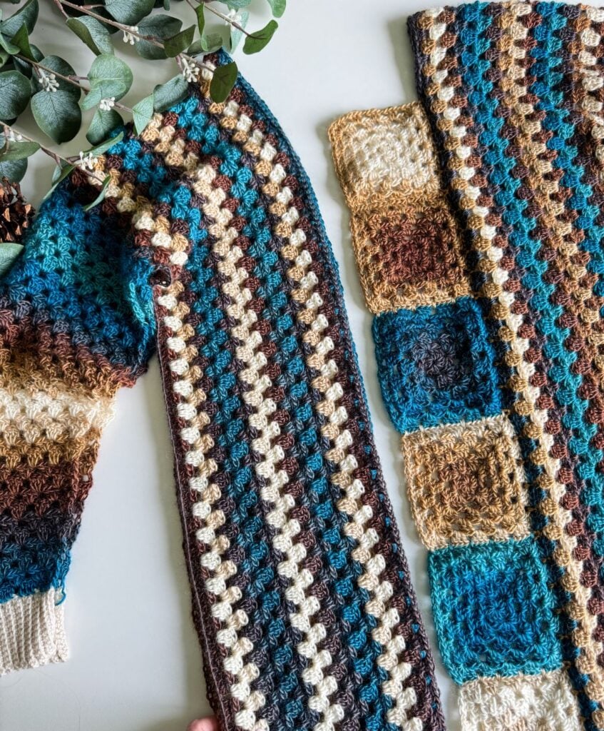 A close-up of two crocheted textiles in earthy tones, one with stripes and another with alternating squares, placed next to a sprig of leafy greenery. Imagine crafting a matching crochet cardigan to complete this cozy aesthetic.