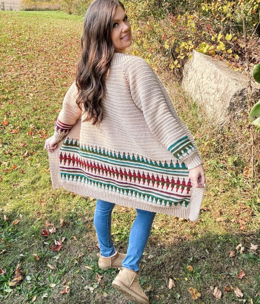 Woman in a mosaic crochet cardigan stands outdoors on grass, showing the back of the sweater.