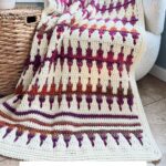 A colorful crochet blanket with a geometric pattern is draped over a chair near a woven basket. Text reads: "Mosaic Crochet Blanket Pattern & Video. No Tails technique.